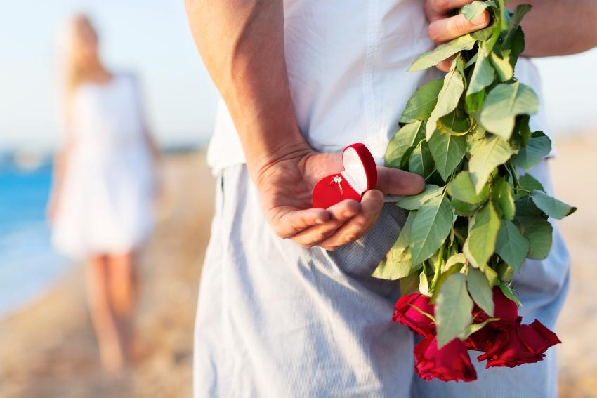 Aufnahme eines Mannes mit Rosen und Verlobungsring hinter dem Rücken