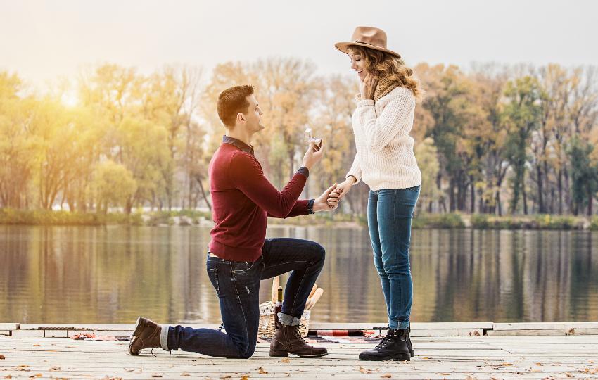 Mann macht Frau knieend einen Heiratsantrag am See