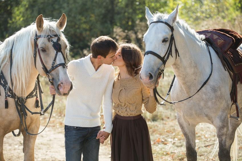 Junges Paar küsst sich zwischen zwei Pferden stehend