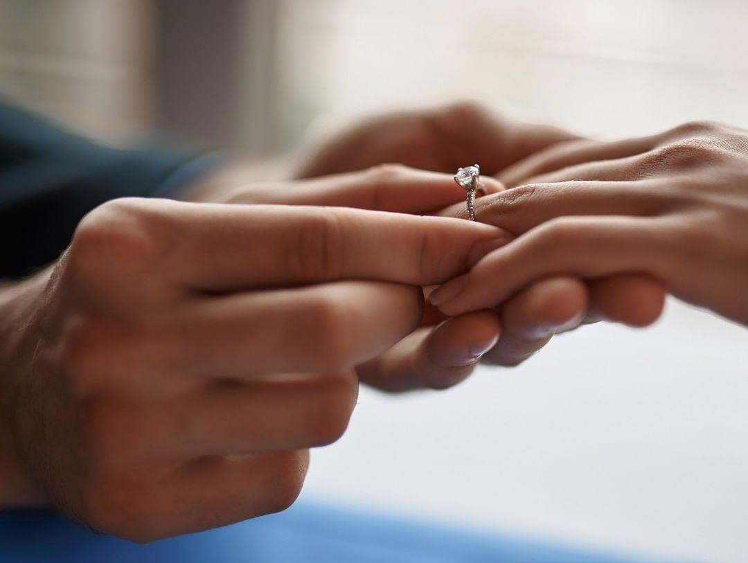 Mann steckt Verlobungsringer an Finger der Frau - Heiratsantrag im Restaurant
