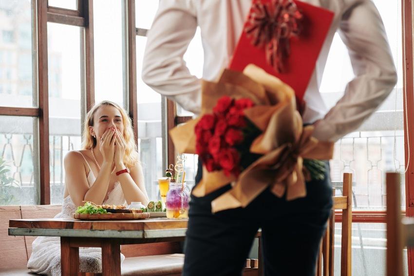 Mann mit Rosen und Geschenk hinter seinem Rücken - HOchzeitsantrag im Restaurant