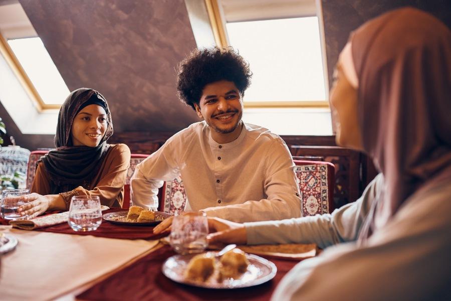 Junges muslimisches Paar sitzt mit weiterer Frau beim Essen und Trinken