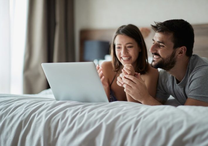 Junges Paar im Bett shoppt online - Wann Eheringe kaufen?